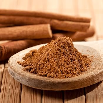 Cannella in Polvere su un cucchiaio di legno, circondata da stecche di cannella, ideale per ricette dolci e salate.